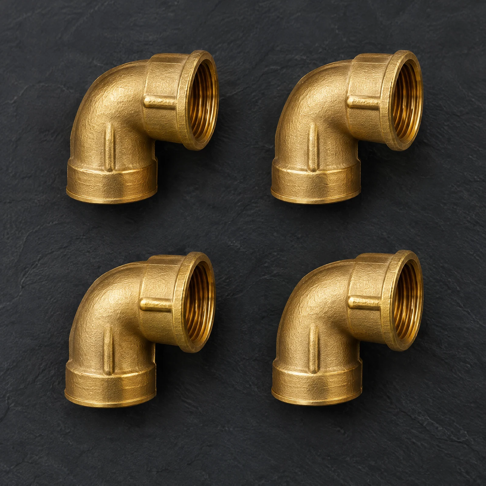Four gold-tone right-angle pipe elbows with female threaded ends arranged on a dark slate surface