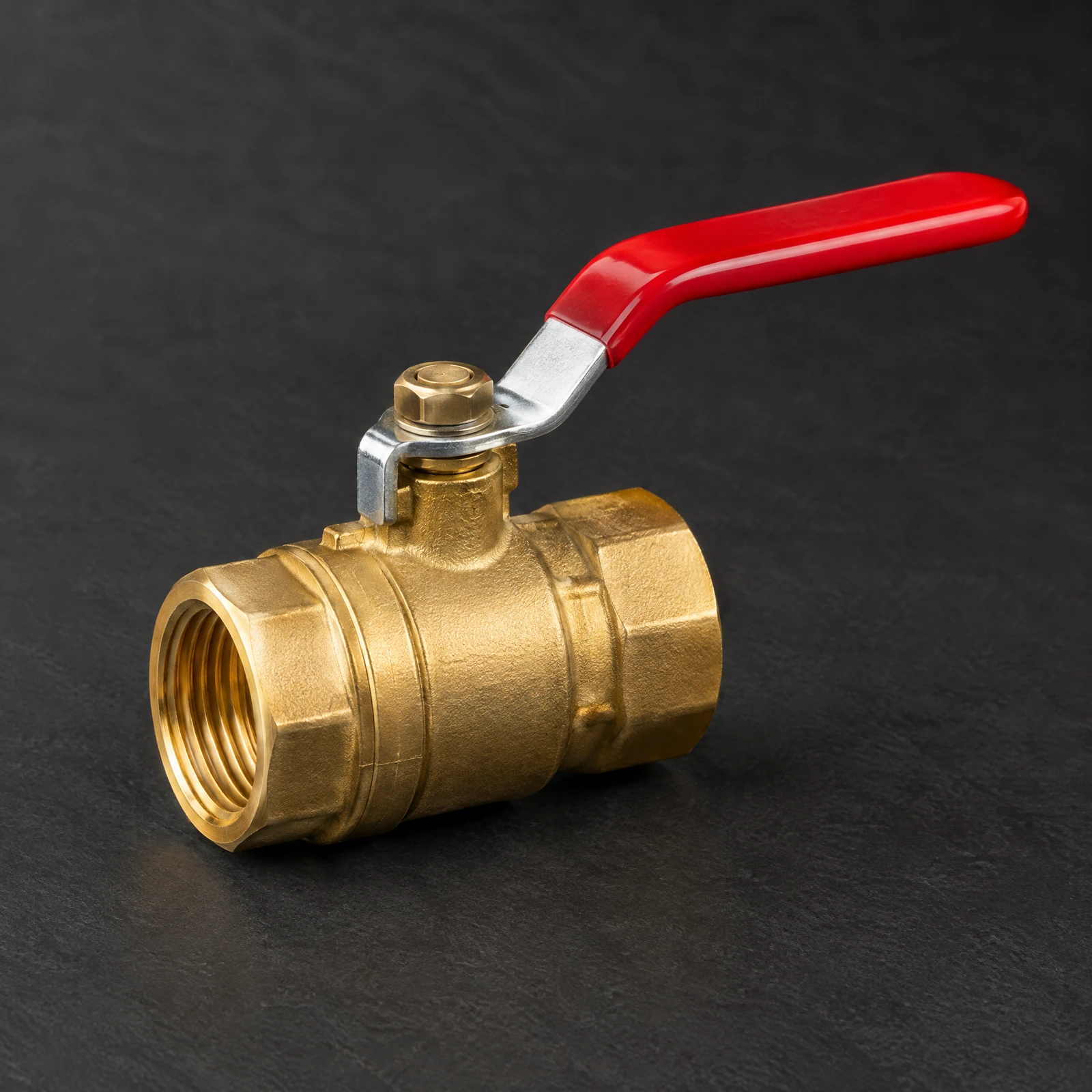 Gold-tone ball valve with a red lever handle and female threaded ends on a dark slate backdrop
