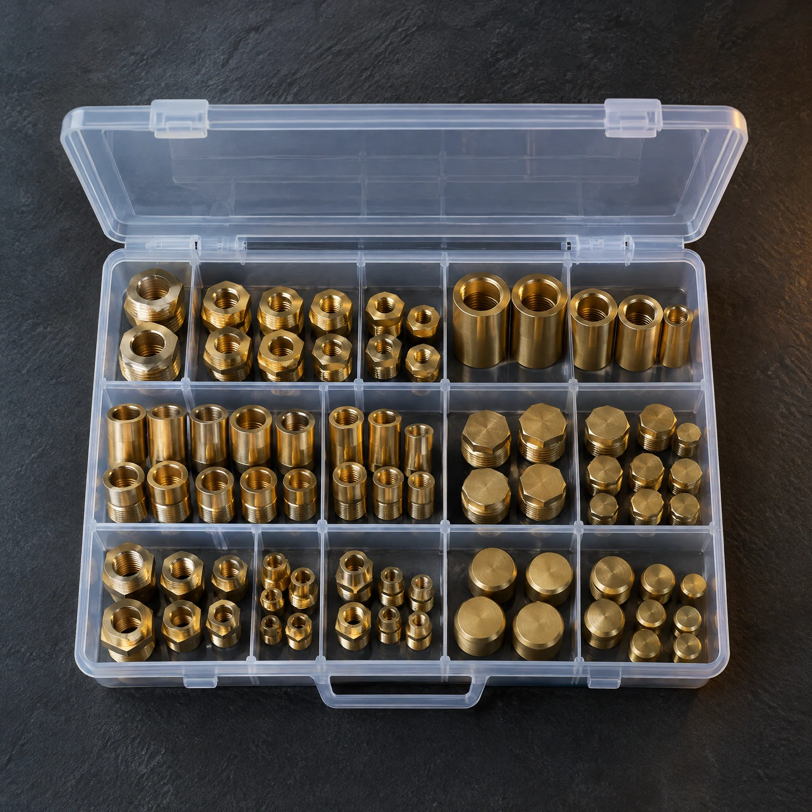 Open clear case with fifteen compartments of brass-colored hex bushings, couplings, plugs and caps on a dark slate surface